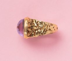 Een 18 karaat gouden ring, met een grote cabochon geslepen amethist gezet in een bezel zetting, met een fijn geciseleerde gedecoreerde scheen met eiken- en olijftakken, Frankrijk. gewicht: 6.87 gram ringmaat: 17 mm / 6.5 US
