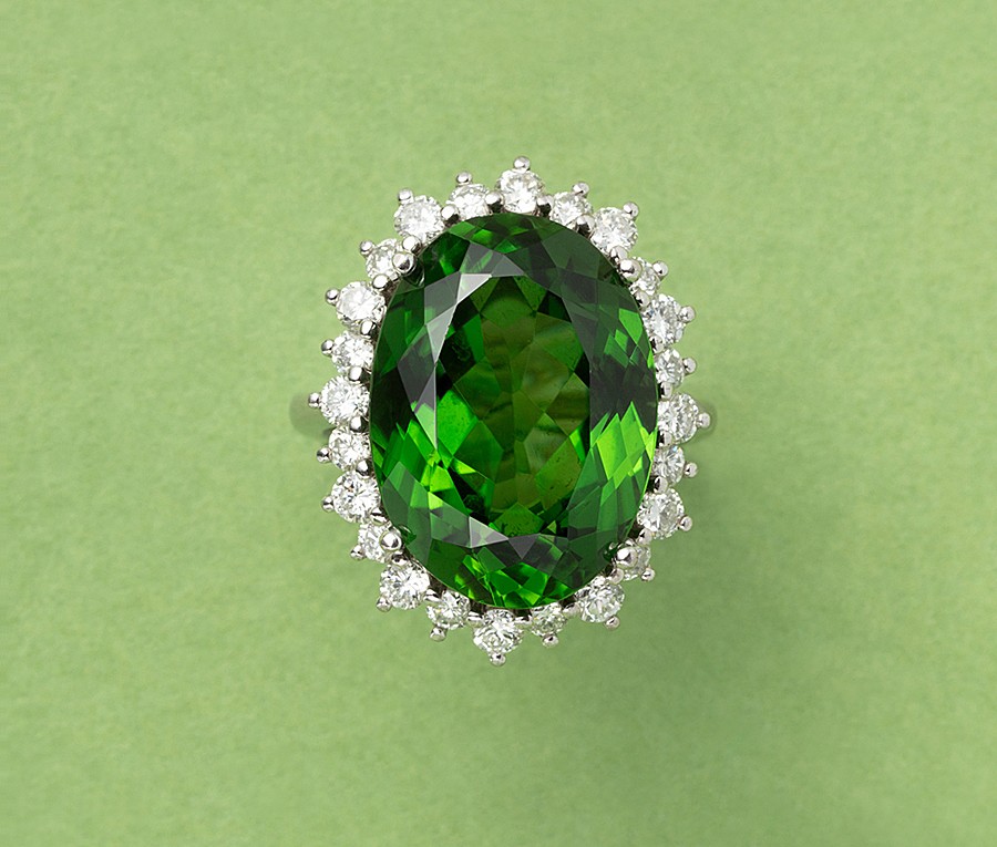 An 18 carat white gold ring set with a large oval facetted green tourmaline (app. 14.00 carat with an entourage of brilliant cut diamonds (0.05 carat each, colour FG, Vs, gem erport AEL-Arnhem). weight: 11.5 gram ring size: 16.25 mm