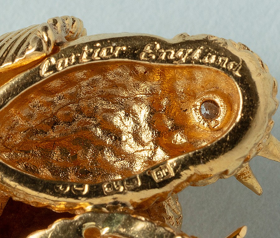 Een 18k gouden broche voorstellende een mandje met vier vogeltjes, de oogjes bezet met robijn, saffier, smaragd en diamant gesigneerd en genummerd: Cartier London en Cartier, L607 met meesterteken JC. gewicht: 14.92 g afmetingen: 2.5 x 3 cm