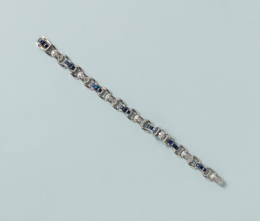 Een art deco platina armband met platte platina schakels die aansluiten op 14 halfronde schakels afwisselend bezet met drie saffieren (21 in totaal met een gewicht van 4.41 crt) en met drie briljant gslepen diamanten (21 met een gewicht van ca. 1.47 crt), met een onzichtbaar slot met het meesterteken voor: J & L Hartzberg, America, New York, circa 1930. gewicht: 29.46 g lengte: 17 cm past bij een polsmaat van 14-16 cm afmetingen schakels: 10 x 5 x 4 mm