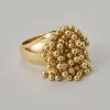 Een brede 18-karaats geelgouden ring met steeds vier bewegende balletjes op een gouden staafje, in een kogelconstructie, aan sliertjes, gesigneerd, genummerd en gedateerd: Cartier, 50731, 1999, model "Perruque" met Frans meesterteken. gewicht: 36.43 g ringmaat: 16.75 mm / 6 1/4 US breedte: 7 - 31 mm